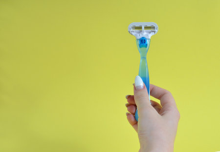 Blue razor in hands on a yellow background.の写真素材