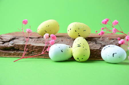 Easter eggs in yellow and green on a wooden stand. Green background. Pink flowers.