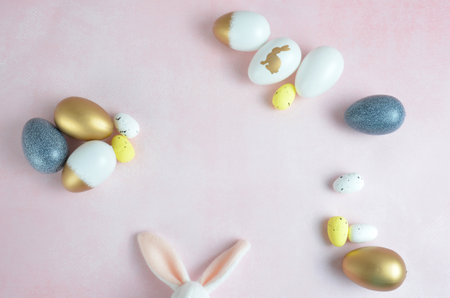 Easter eggs are yellow, dark blue, white and gold. Pink background. Easter. Bunny ears.