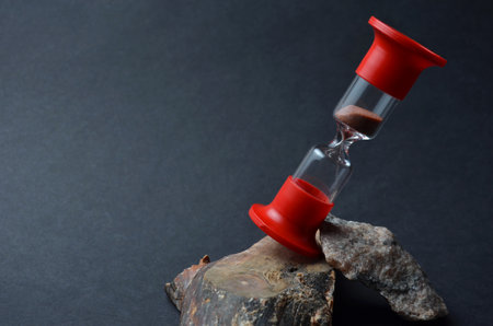 Red hourglass close-up on a black background. Sea stones and wood.の写真素材