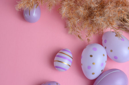 Easter eggs of purple color with patterns and dry grass on a pink background. Easter
