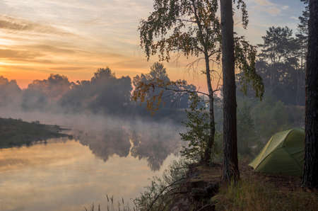 Camping tent near tree with morning fog over river. Travel, leisure and tourism in nature.の写真素材