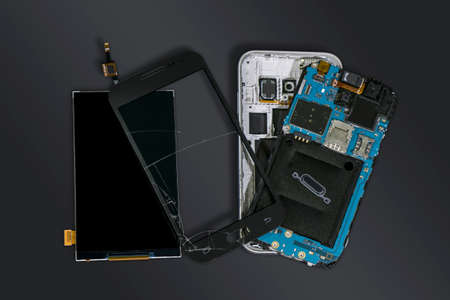 Dismantled mobile phone with broken display screen isolated on dark grey backgroundの写真素材