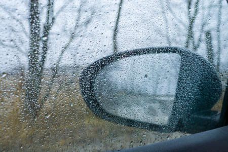 Drops on the glass window of car. Dramatic blurry background of street rainの写真素材