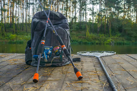 Fishing background of spinning rod with reel and landing net on wood boards on lake in forestの写真素材