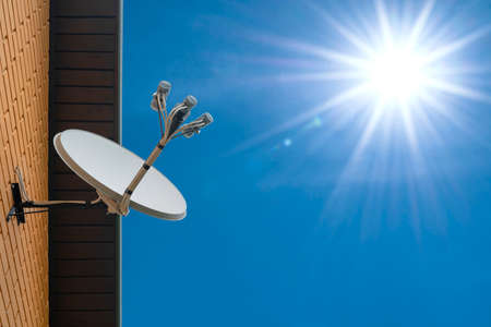 Satellite dish antenna mounted on the wall of a private house on blue sky backgroundの写真素材