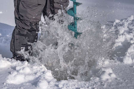 Winter fishing concept. Fisherman in action. Some one is making the hole in snowy ice at lake by ice screwの写真素材