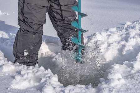 Winter fishing concept. Fisherman in action. Some one is making the hole in snowy ice at lake by ice screwの写真素材