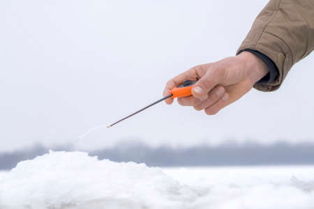 Winter fishing concept. Hand of fisherman with specialised rod above snowy ice.の写真素材