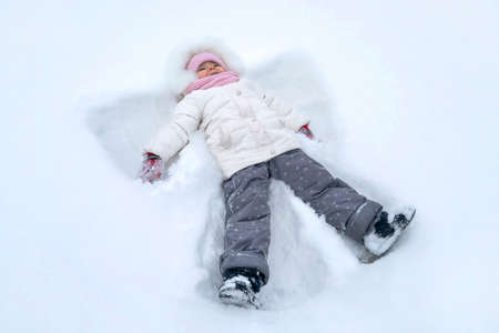 Cute girl child makes snow angel at winter park