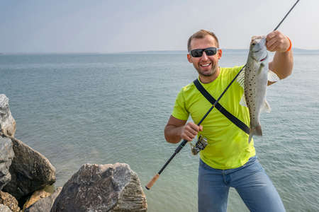Seabass fishing. Fisherman with sea bass fish. Man with fishing tackle at coast line