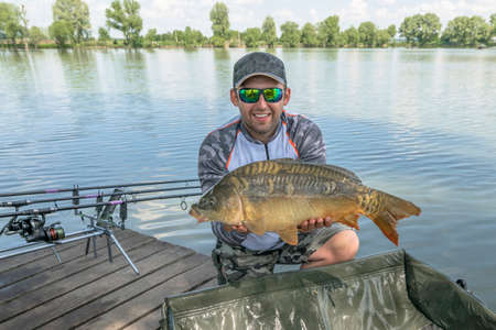 Carp fishing. Fisherman with fish trophy in hands at lake