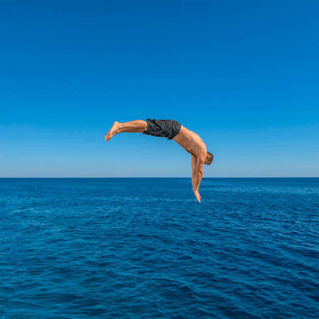 Fly after jump. Man jumping in blue sea water for dive. Summer fun lifestyleの写真素材