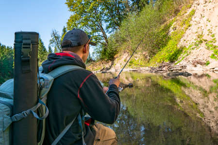 Fishing at wild mountain river. Fisherman catch trout fish at stone coast of forest stream