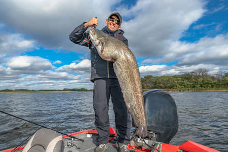 Success catfish fishing. Happy fisherman with big sheatfish trophy at boat