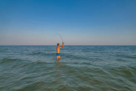 Fisherman in water make cast. Summer fishing on the sea. Vacation leisure.の写真素材