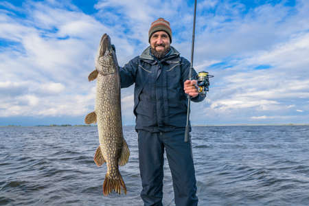 Successful pike fishing. Happy fisherman hold huge muskie fishの写真素材