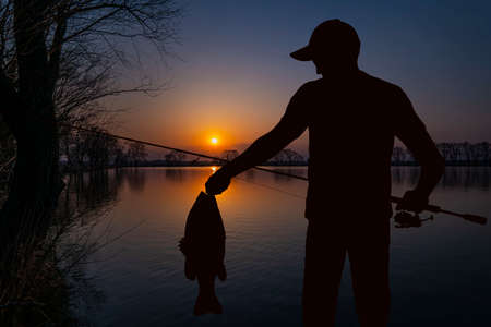Night evening fishing. Fisherman silhouette on sunset landscapeの写真素材