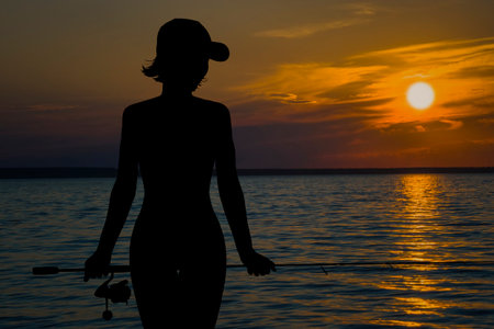 Night evening fishing. Fisherman silhouette on sunset landscapeの写真素材