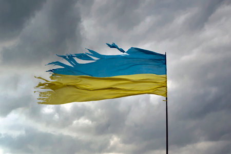Tattered shabby Ukraine flag on gray cloudy sky as a symbol of nation struggle and courage
