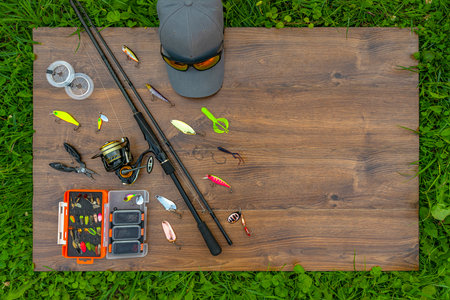 Spinning fishing tackle set. Spinning rod with reel, lures, baits, spoon, spinner, hooks, cap, sunglasses on wooden platformの写真素材