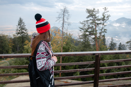 Hipster girl enjoying view of the mountains from the observation platform. Travel girl with backpack and orange hat.の写真素材