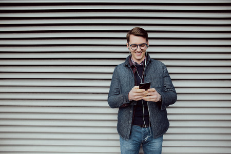 A young boy is browsing the internet on a smartphone and listen to music with headphones.