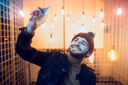 Happy hipster guy making selfie photo against the background of lamps.の写真素材
