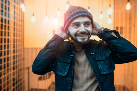Happy hipster guy against the background of lamps. Holds his hands to the hat.の写真素材