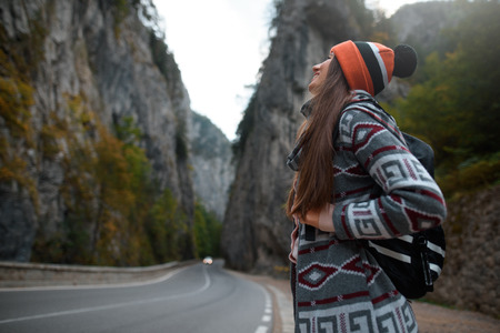 Smiling young girl with a backpack near a road in the mountains. Looks up at landscape.の写真素材