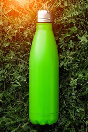 Stainless  water bottle, light green color. Mockup isolated on green grass background with sunlight effect. Glossy aluminum vacuum thermo tumbler flask.の写真素材