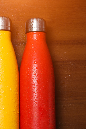 Colorful stainless  bottles, on a wooden table sprayed with waterの写真素材