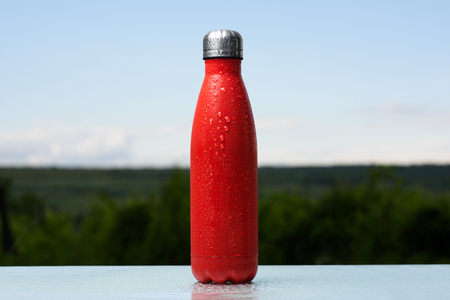 Stainless bottle, sprayed with water. Sky and forest on background. On the glass desk.の写真素材