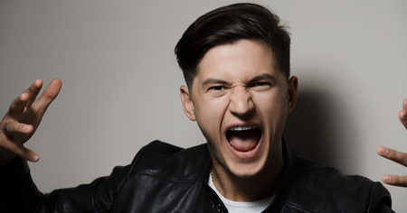 Portrait of emotional screaming young guy, background of grey