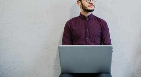 Young pensive guy using laptop, wearing glasses on background of white.の写真素材