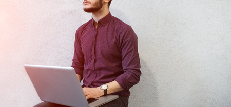 Young pensive guy using laptop, wearing glasses on background of white.の写真素材