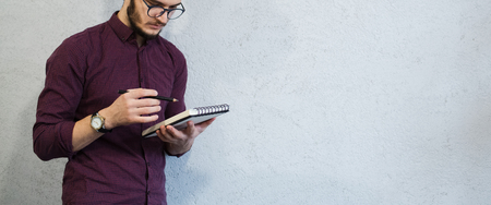 Young guy holding pencil and notebook, wearing glasses, on abckground of white.の写真素材