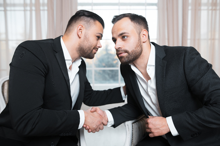 Businessmen shaking hands at the meeting over background of window, sitting on armchairs.の写真素材