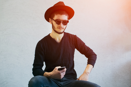 Portrait of bearded hipster guy wearing sunglasses with smartphone in hands over white backgroundの写真素材