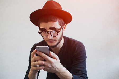 Portrait of young man with smartphone in hands, wearing black hat and sunglassesの写真素材
