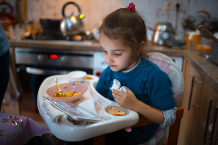 Baby girl eating and watch tablet in kitchen room.の写真素材