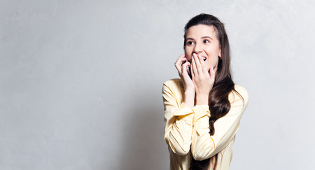Portrait of young surprised girl talking on smartphone, dressed in yellow, over white background.