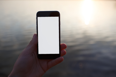 Holding smartphone in hand over sunset with mockup.の写真素材