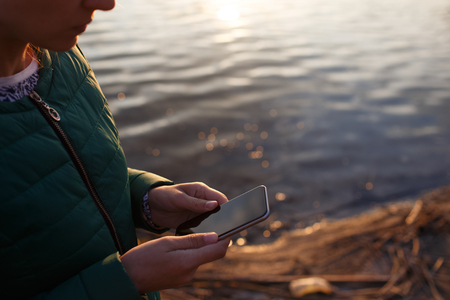 Holding smartphone in hand over sunset background.の写真素材