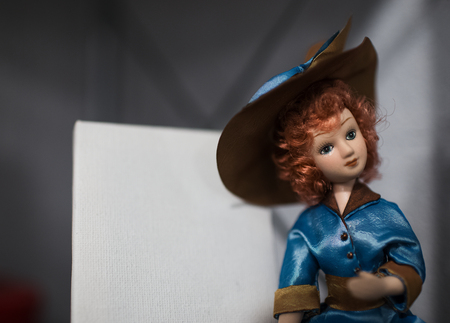Portrait of porcelain doll with red curly hair, wearing blue dress and hatの写真素材