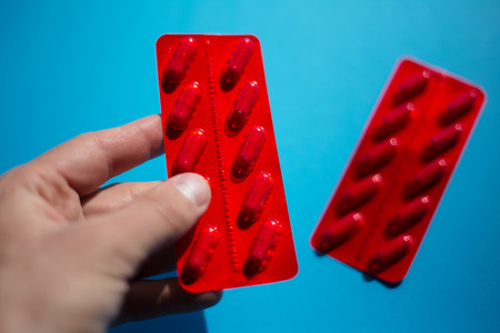 Handing medicine pills capsules, red pack over blue.