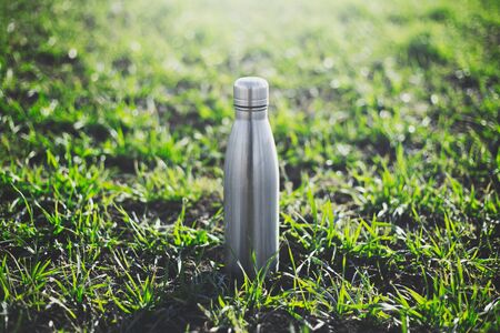 Reusable steel thermo water bottle on green grass.	