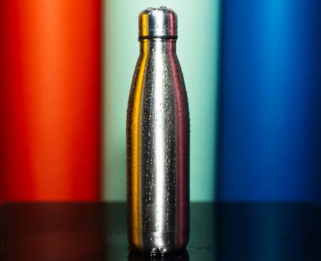 Close-up of reusable steel thermo bottle sprayed with water on background of lush lava, aqua menthe and phantom blue of color.の写真素材