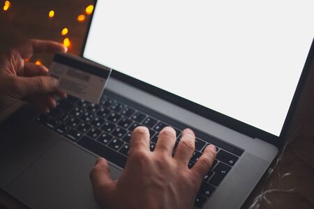 Close-up of male hands using credit card for online purchase by laptop. Dark room with garlands.の写真素材