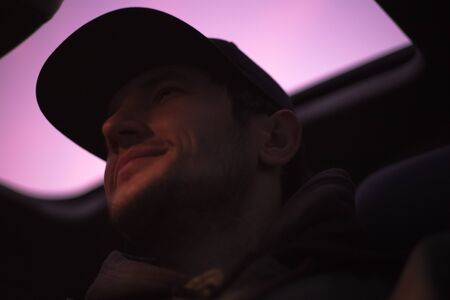 Dark portrait. Down view of young smiling hipster inside car on background of sunroof.の写真素材